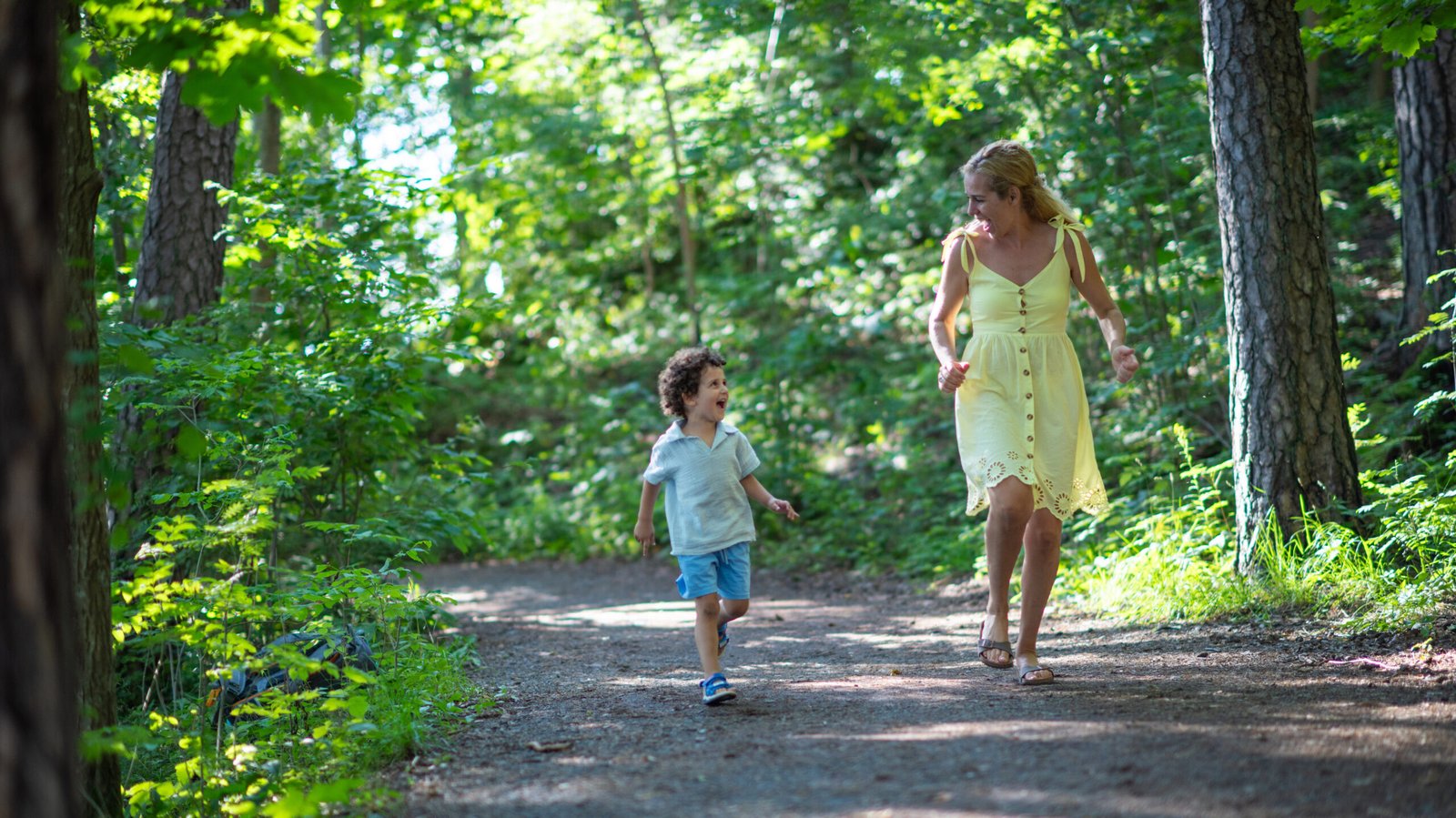 Cute little boy and his mother running on a dirt road in forest.